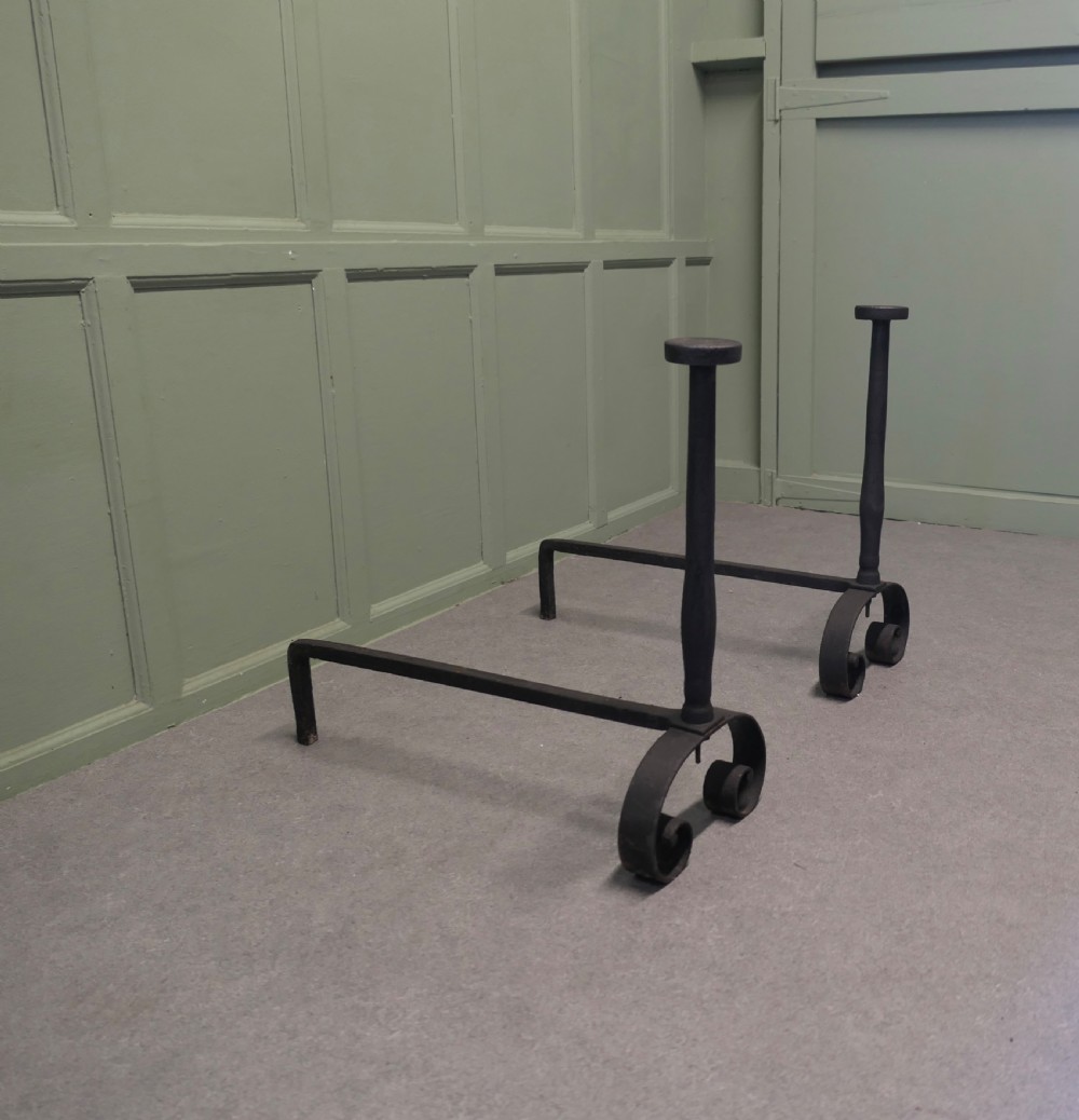 A pair of tall dark iron andirons featuring scrolled pedestal bases and vertical upright pillars with flat caps. View III
