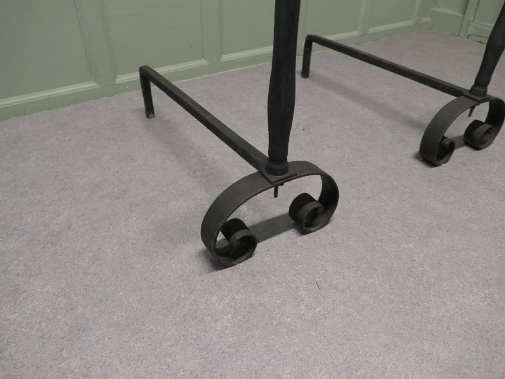 A pair of tall dark iron andirons featuring scrolled pedestal bases and vertical upright pillars with flat caps. View IV