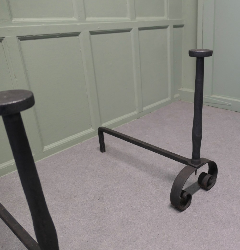 A pair of tall dark iron andirons featuring scrolled pedestal bases and vertical upright pillars with flat caps. View V