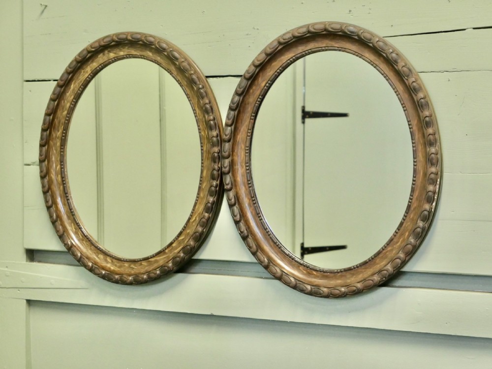 A pair of matching oval wall mirrors featuring carved egg-and-dart borders with a brown simulated wood grain paint finish.