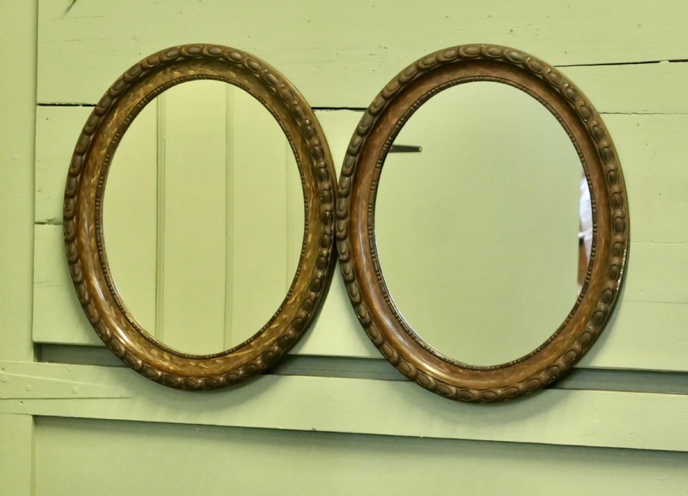 A pair of matching oval wall mirrors featuring carved egg-and-dart borders with a brown simulated wood grain paint finish. View V