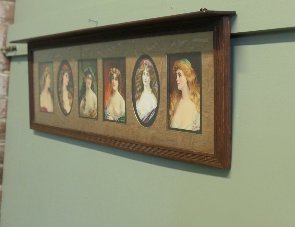A horizontal dark oak wall shelf featuring six mounted Pre-Raphaelite style female portraits set behind alternating rectangular and oval apertures. View IV