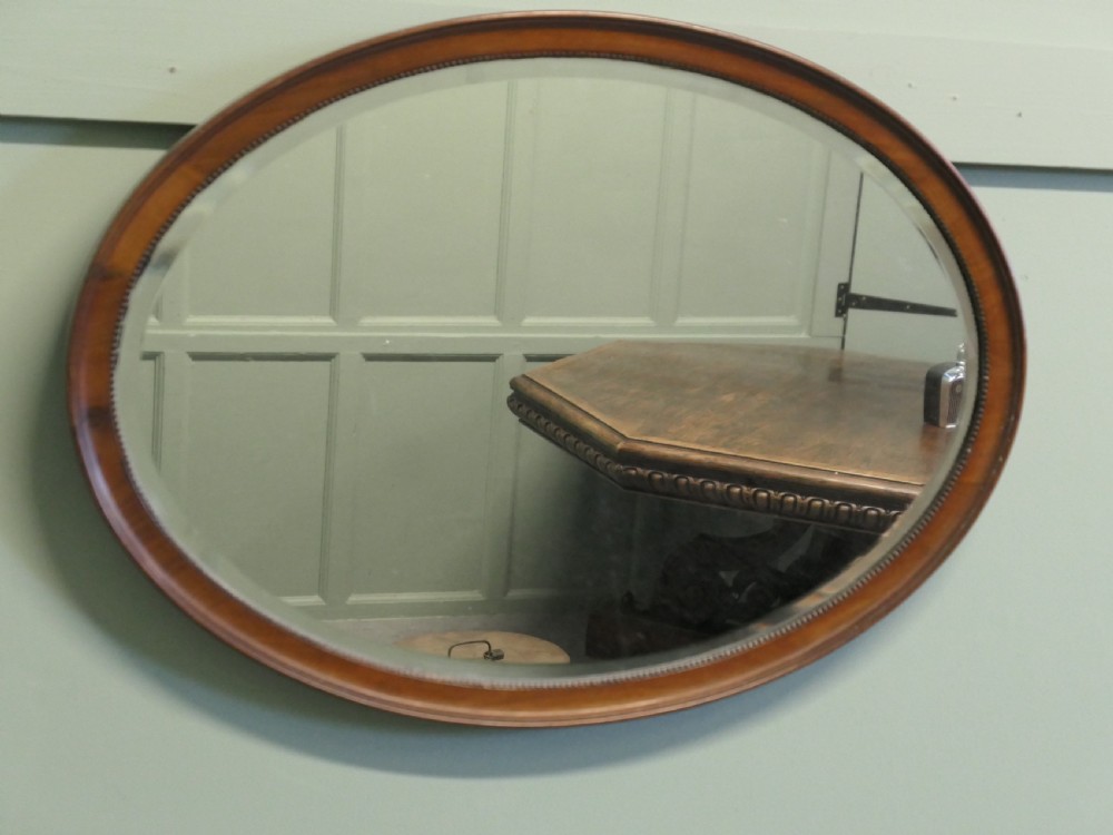 A horizontal oval wall mirror with a mahogany wooden frame featuring a bevelled glass edge and beaded inner trim.