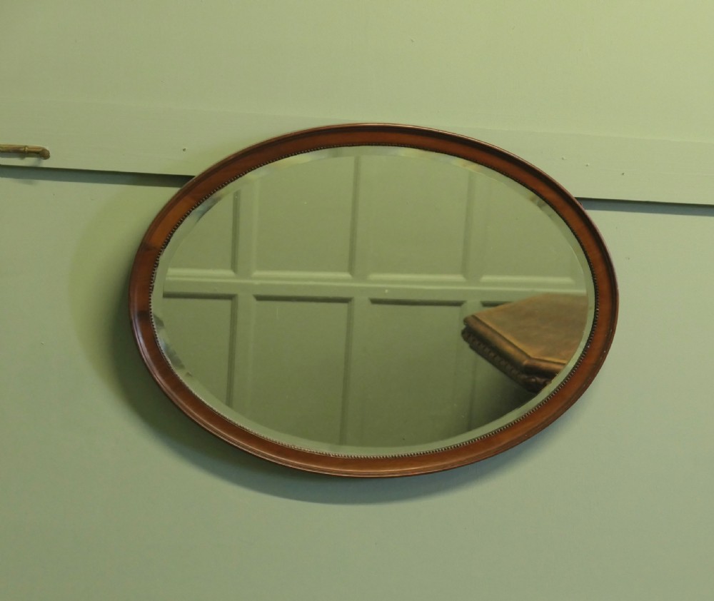A horizontal oval wall mirror with a mahogany wooden frame featuring a bevelled glass edge and beaded inner trim. View II