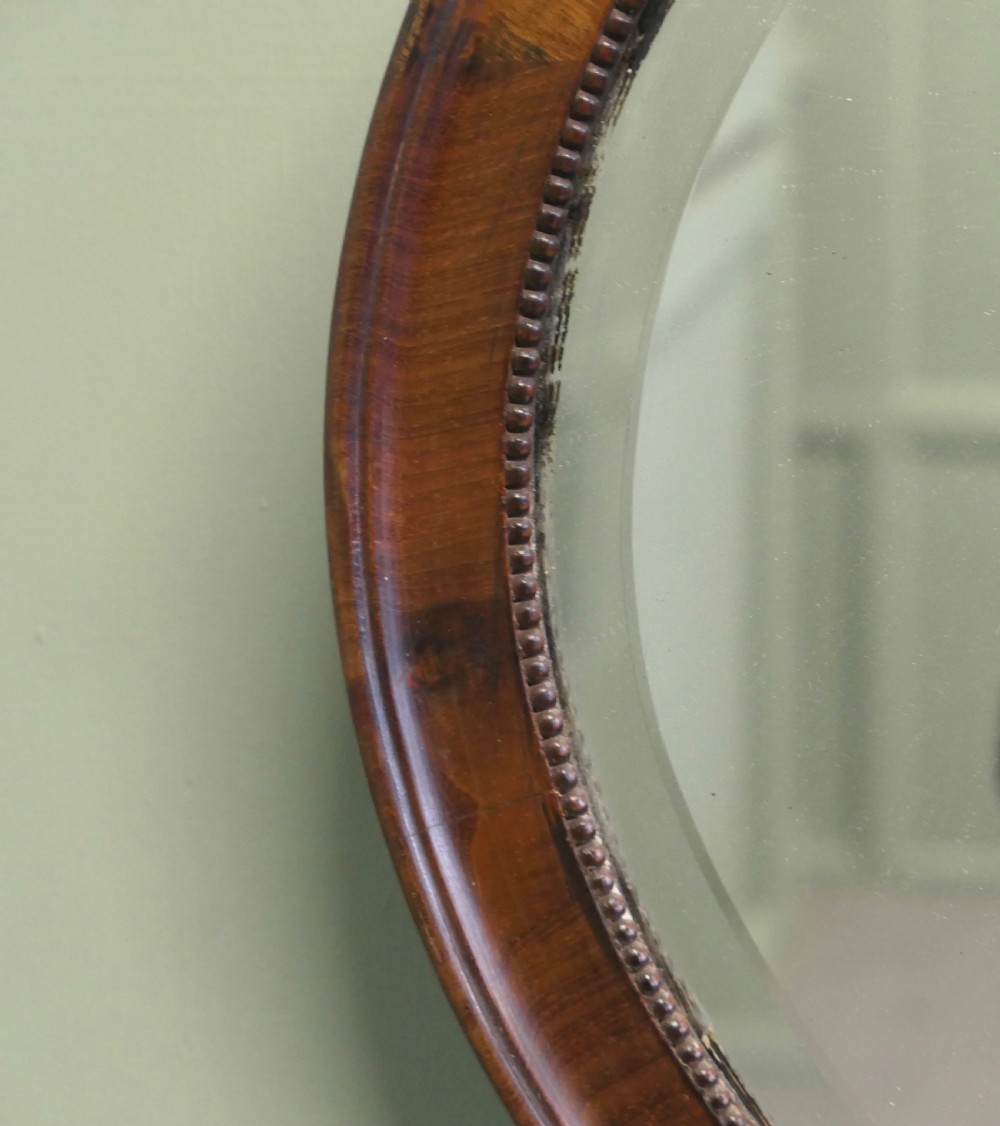 A horizontal oval wall mirror with a mahogany wooden frame featuring a bevelled glass edge and beaded inner trim. View III