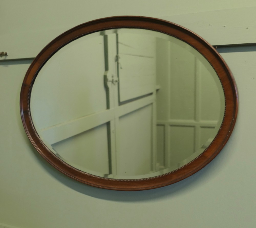 A horizontal oval wall mirror with a mahogany wooden frame featuring a bevelled glass edge and beaded inner trim. View IV