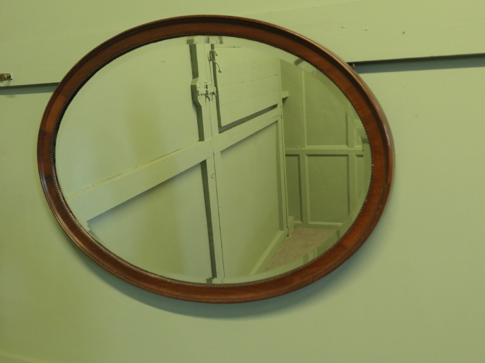 A horizontal oval wall mirror with a mahogany wooden frame featuring a bevelled glass edge and beaded inner trim. View V