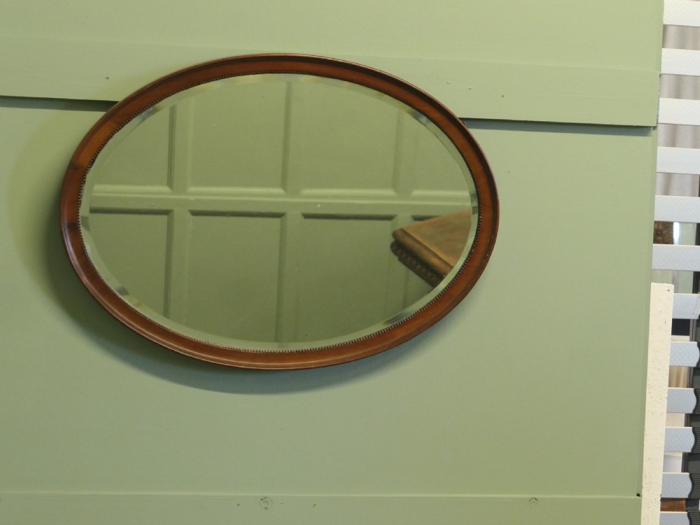 A horizontal oval wall mirror with a mahogany wooden frame featuring a bevelled glass edge and beaded inner trim. View VI