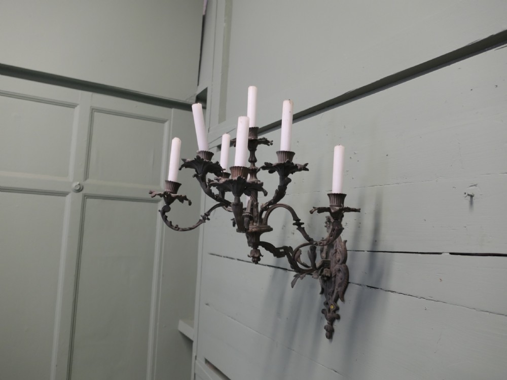 A seven-arm cast bronze wall sconce featuring scrolling foliate branches and candle holders mounted on an ornate vertical backplate.