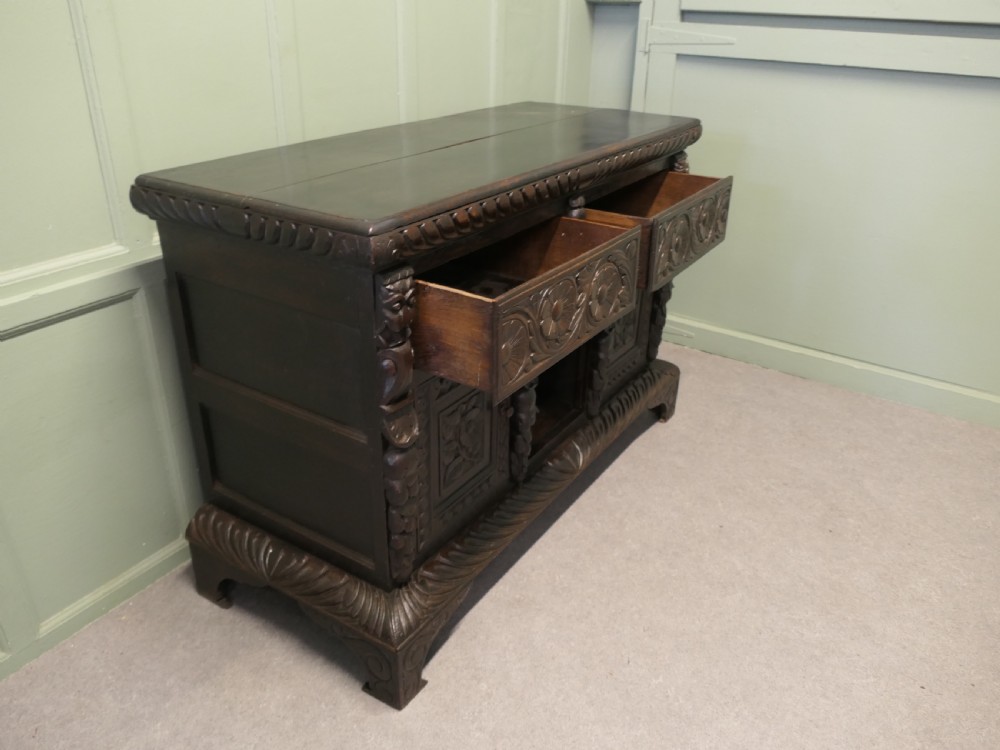 A dark carved oak dresser base featuring Green Man masks, floral panels, and gadrooned borders. View II
