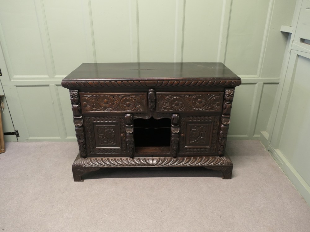 A dark carved oak dresser base featuring Green Man masks, floral panels, and gadrooned borders. View III