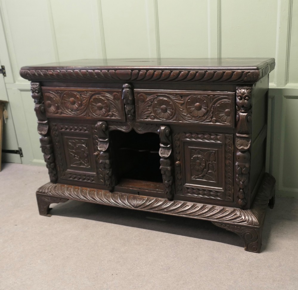 A dark carved oak dresser base featuring Green Man masks, floral panels, and gadrooned borders. View IV