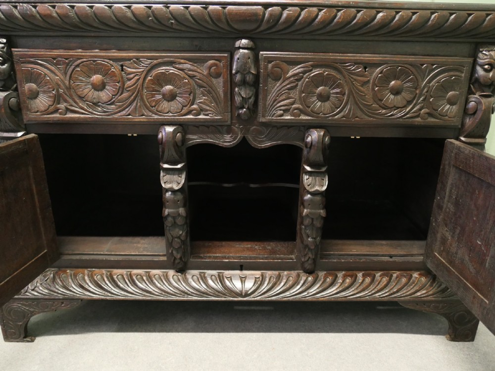 A dark carved oak dresser base featuring Green Man masks, floral panels, and gadrooned borders. View VI