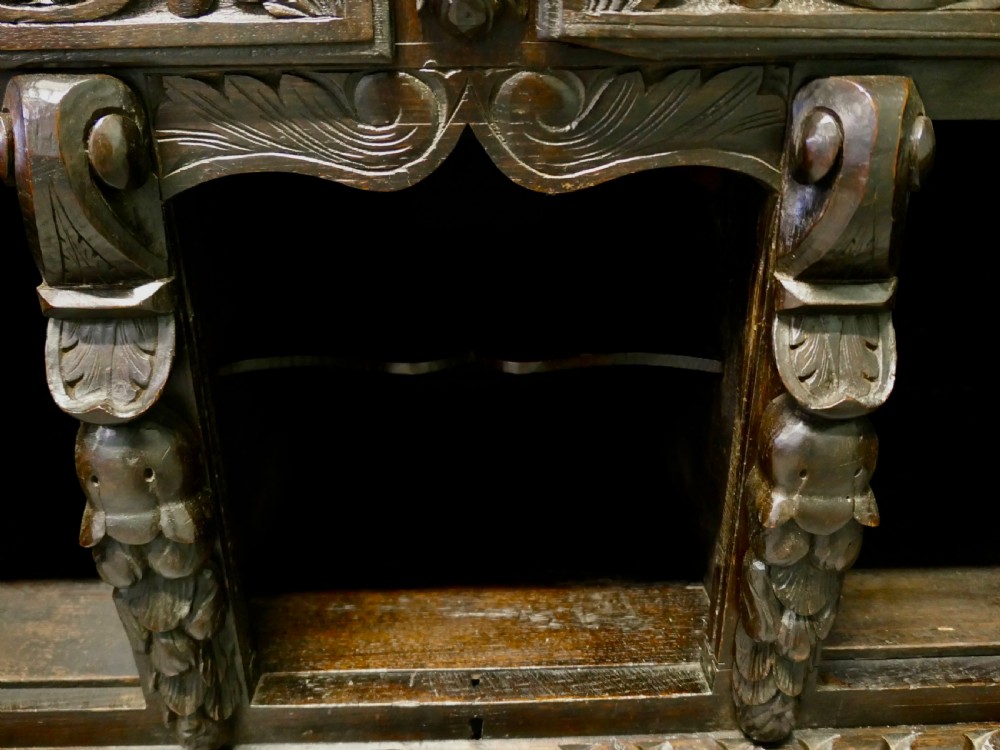 A dark carved oak dresser base featuring Green Man masks, floral panels, and gadrooned borders. View VII
