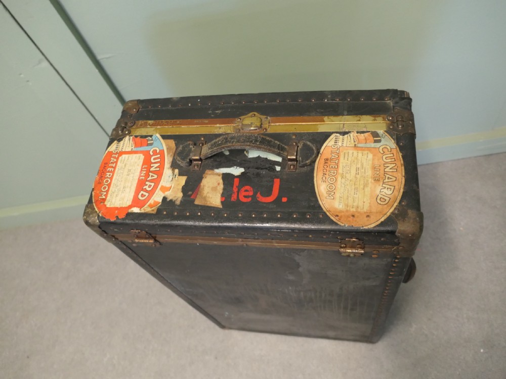 A black canvas cabin trunk featuring brass latches, riveted edges, a central handle, and original Cunard Line Cherbourg travel labels. View II