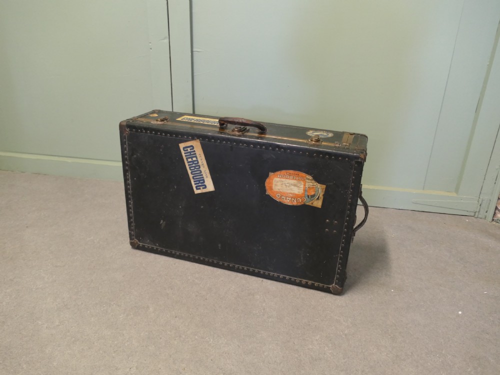 A black canvas cabin trunk featuring brass latches, riveted edges, a central handle, and original Cunard Line Cherbourg travel labels. View V
