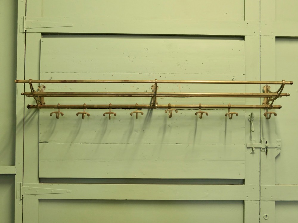 A 5ft French Art Deco brass wall-mounted hat and coat rack featuring an upper slatted shelf rail and eight sliding double hooks.