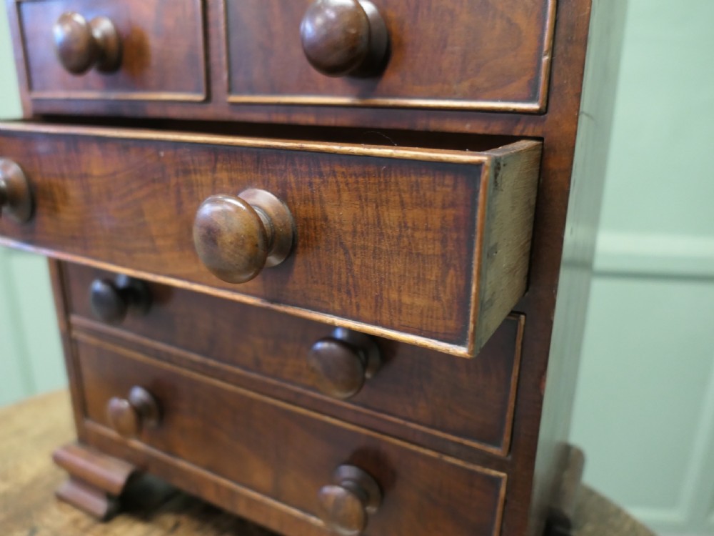 A Victorian mahogany miniature chest of drawers featuring five drawers with fine string inlay, turned wooden knobs, and bracket feet. View II