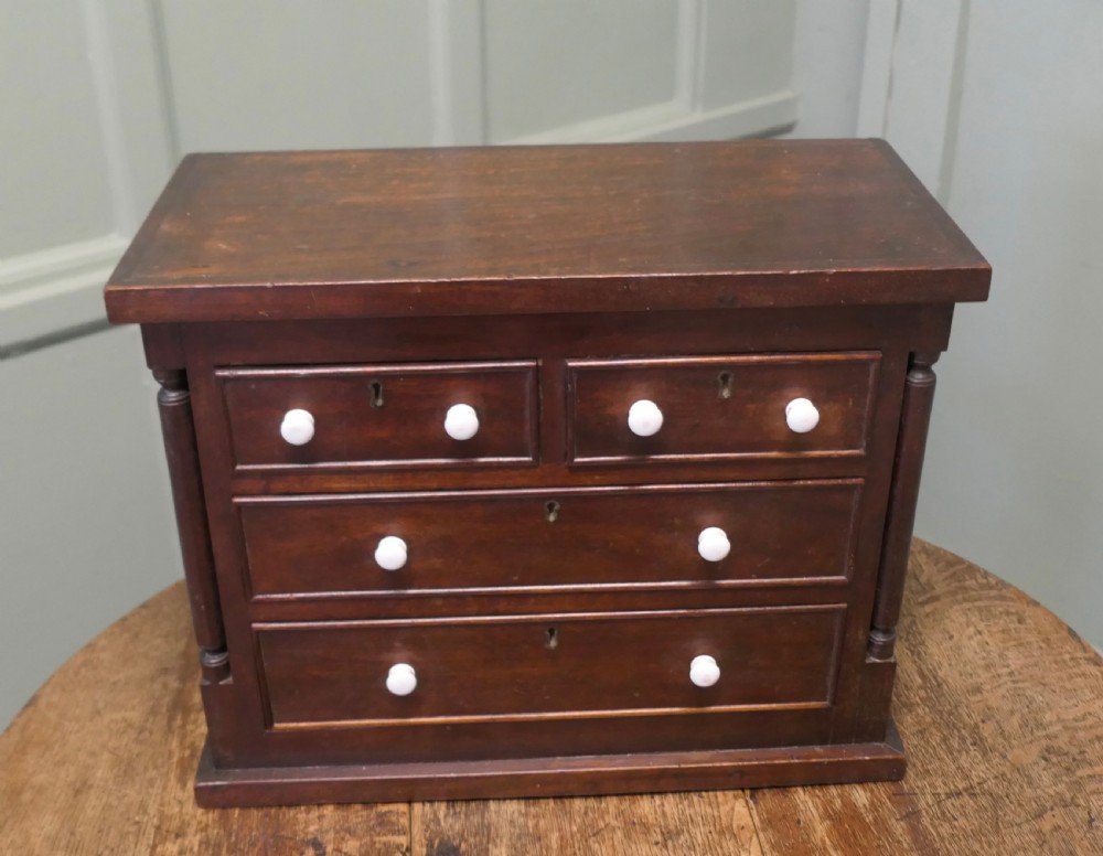A 19th-century mahogany miniature Scotch chest featuring white knobs, side columns, and multiple drawer tiers.
