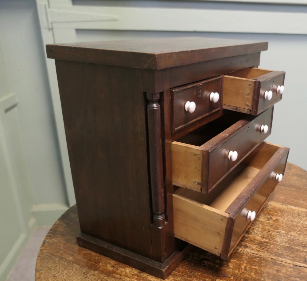 A 19th-century mahogany miniature Scotch chest featuring white knobs, side columns, and multiple drawer tiers. View V