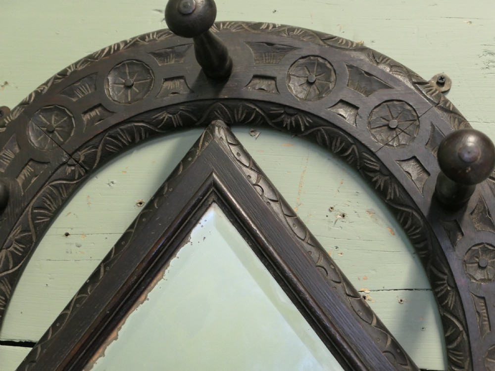 A dark carved oak horseshoe-shaped wall rack featuring five turned wooden coat pegs and a central diamond-shaped mirror. View IV