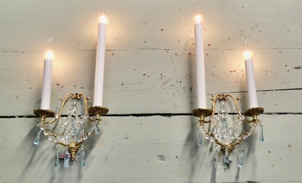 A pair of French gilt brass two-arm wall sconces decorated with clear and blue crystal glass droplets.