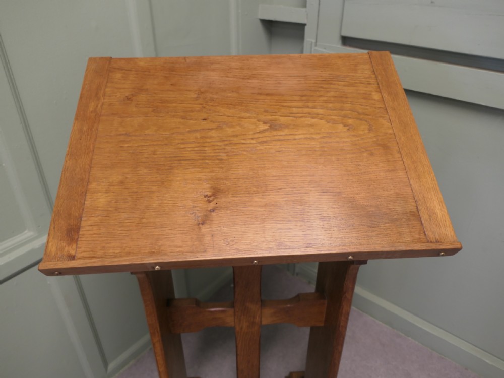 A golden oak Arts and Crafts style lectern featuring a sloped top rest, central pierced cross motif framing, and trestle feet. View V
