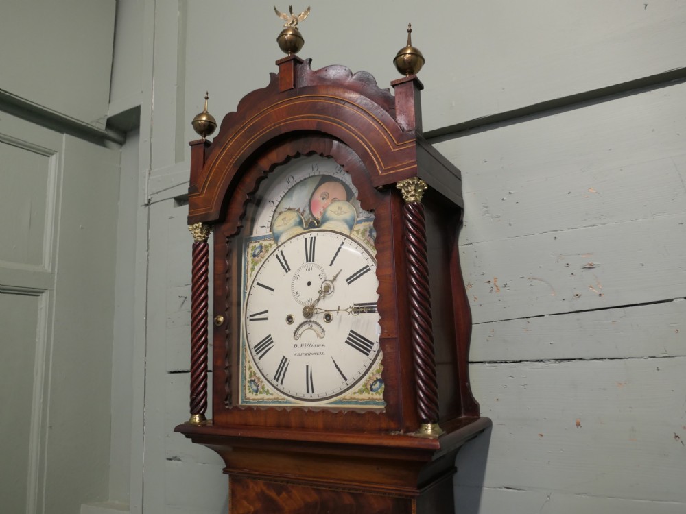 A Georgian mahogany longcase clock with a painted moonphase dial, twisted side columns, brass finials, and flame mahogany inlaid casing. View II