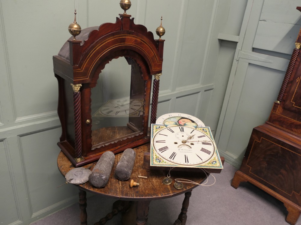 A Georgian mahogany longcase clock with a painted moonphase dial, twisted side columns, brass finials, and flame mahogany inlaid casing. View VI