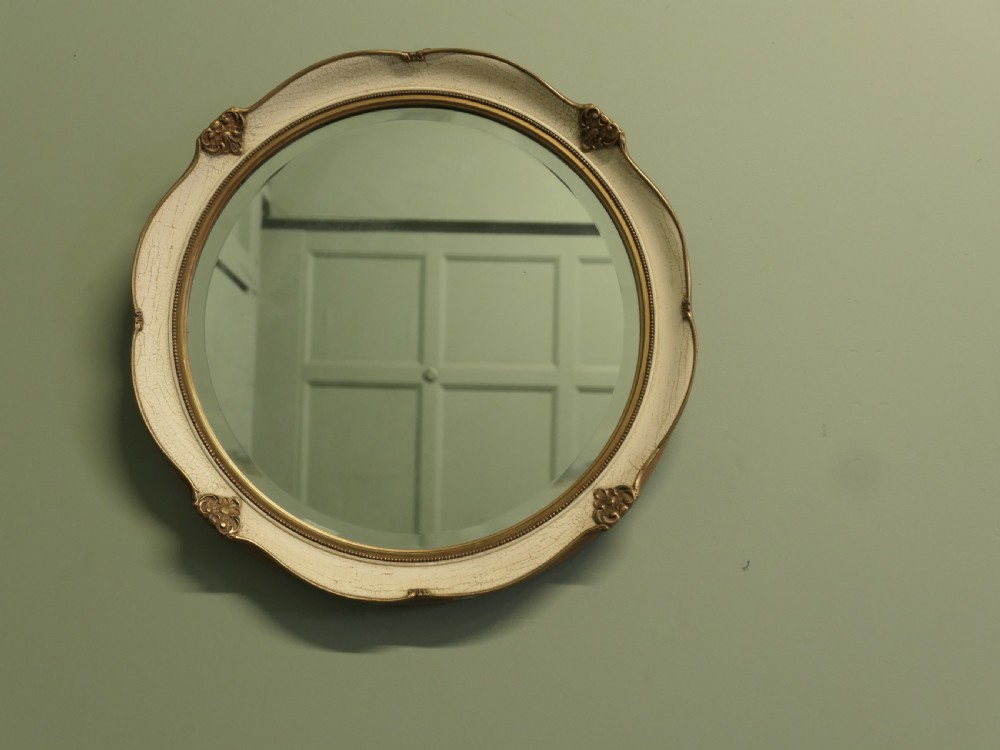 A circular wall mirror featuring a crackle-glazed cream painted frame accented with gilt embellishments and a bevelled glass plate. View V