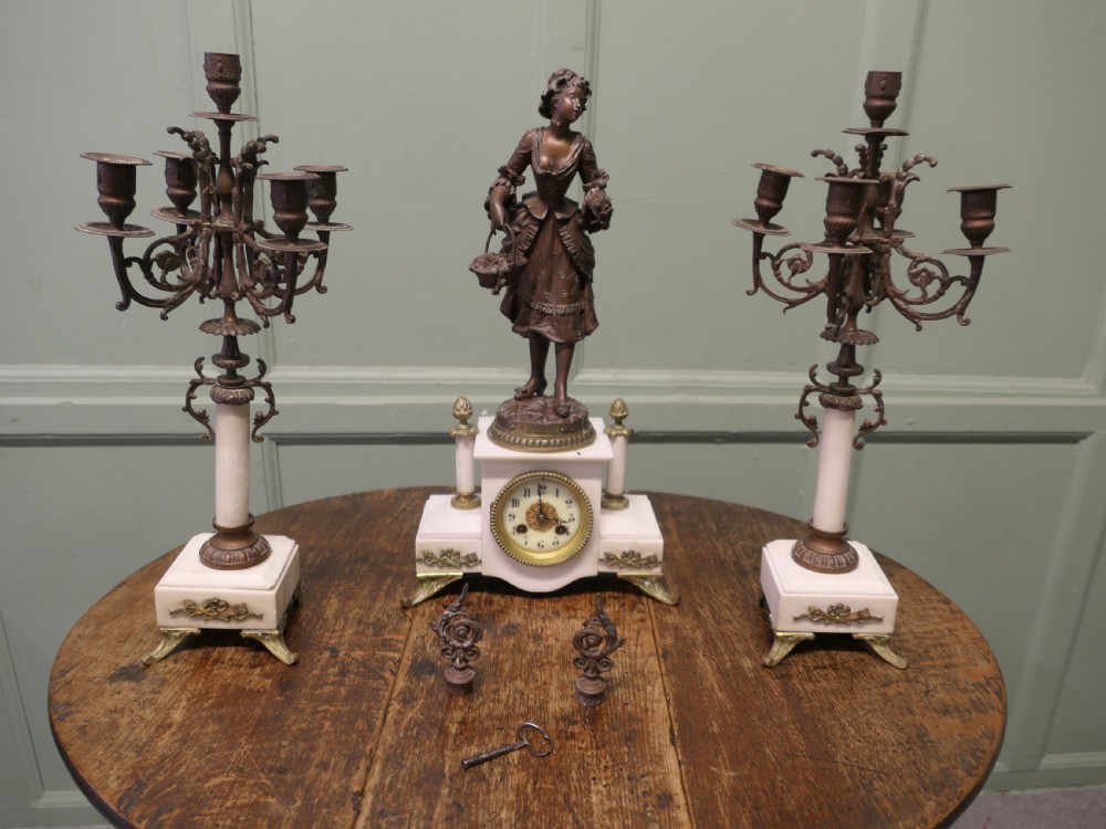 A nineteenth-century French clock garniture set comprising a central bronze sculpture on a marble clock base flanked by two matching multi-arm bronze candelabras.