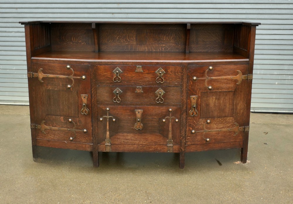 An Arts and Crafts oak sideboard featuring decorative copper strap hinges, heart-shaped drawer pulls, and a low shelf upper gallery.