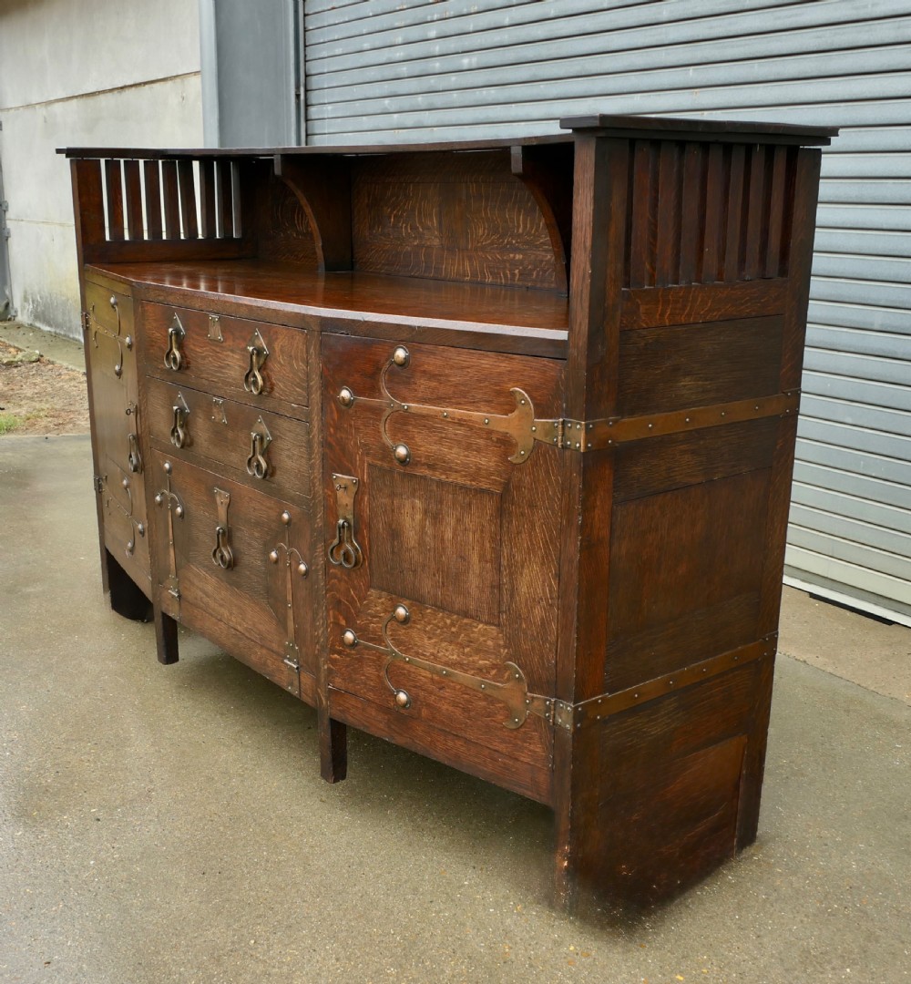 An Arts and Crafts oak sideboard featuring decorative copper strap hinges, heart-shaped drawer pulls, and a low shelf upper gallery. View II
