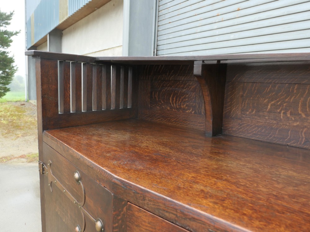 An Arts and Crafts oak sideboard featuring decorative copper strap hinges, heart-shaped drawer pulls, and a low shelf upper gallery. View VI