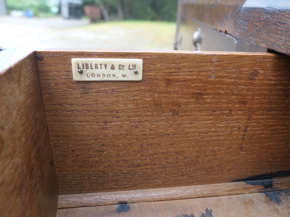 An Arts and Crafts oak sideboard featuring decorative copper strap hinges, heart-shaped drawer pulls, and a low shelf upper gallery. View VII