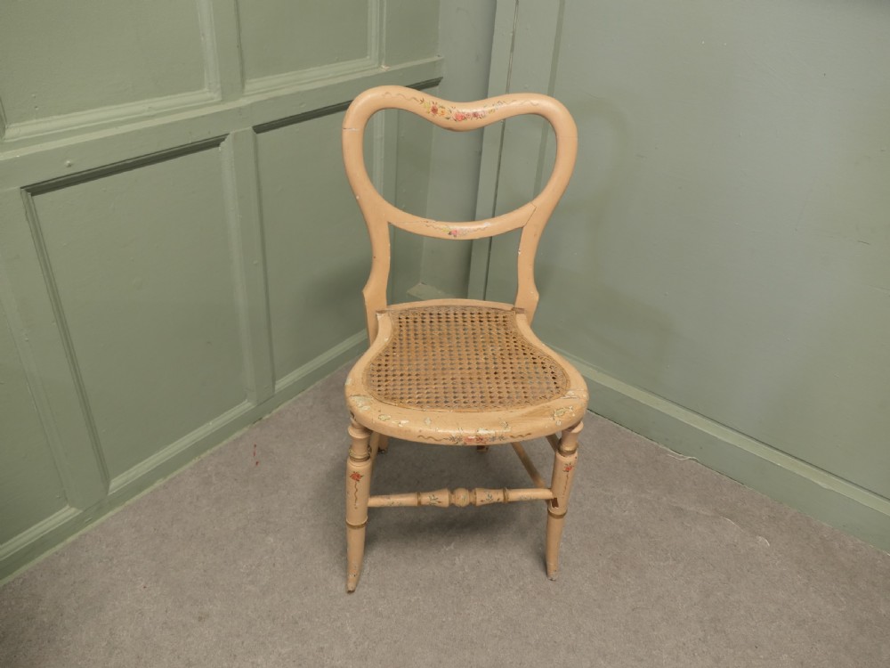 A Victorian painted balloon back bedroom chair featuring a cream frame with hand-painted floral motifs and a woven cane seat.