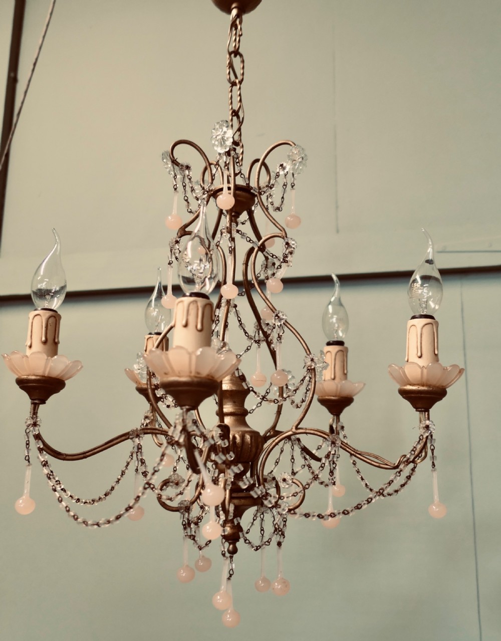 A six-arm gilt metal chandelier featuring frosted floral sconces, hanging pink glass droplets, and delicate beaded crystal swags. View V