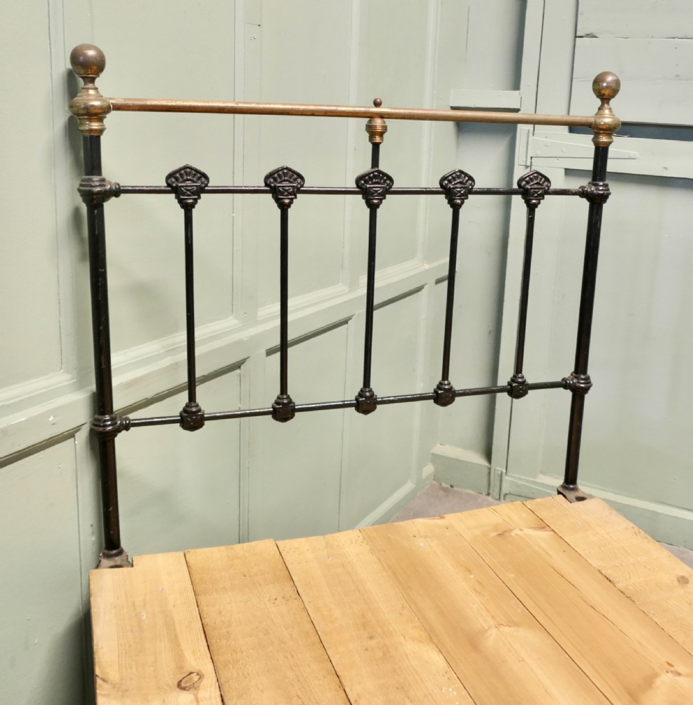 A Victorian single bedstead featuring a black painted iron frame with vertical spindles, brass top rails, brass finials, and a wooden slate base. View II