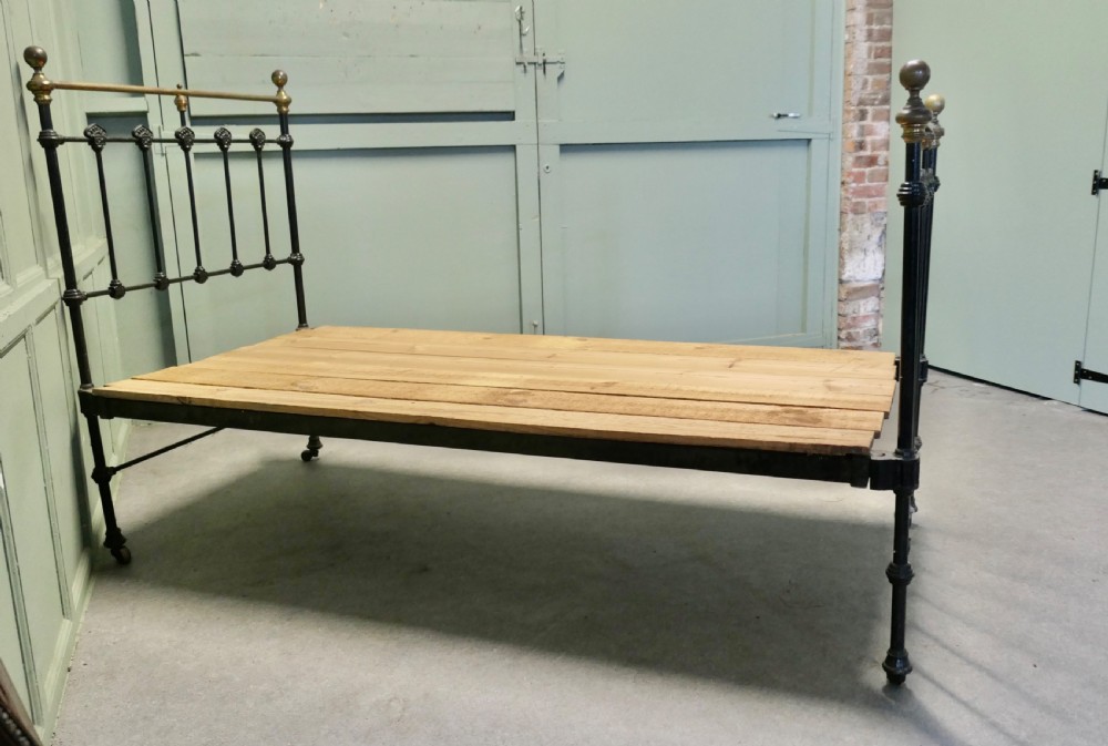 A Victorian single bedstead featuring a black painted iron frame with vertical spindles, brass top rails, brass finials, and a wooden slate base. View III