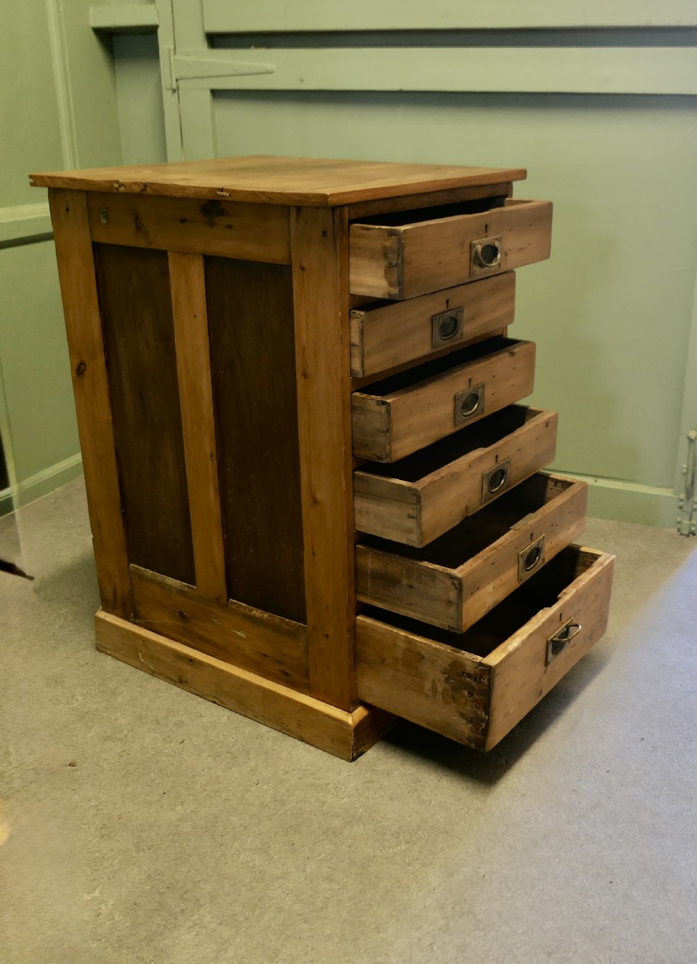 A tall 19th-century pine filing cabinet featuring six shallow drawers with flush brass handles and keyhole escutcheons on a solid plinth base. View V