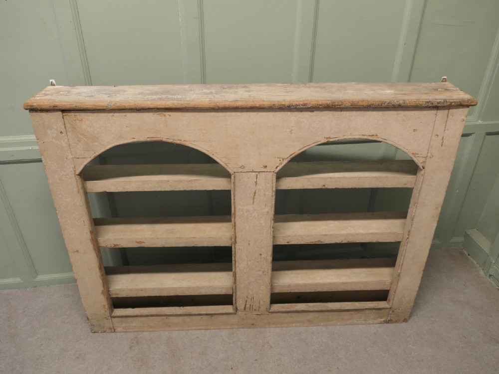 An early 19th-century French pine alcove shelving unit featuring two arched open bays, horizontal interior shelves, and a distressed cream painted finish.
