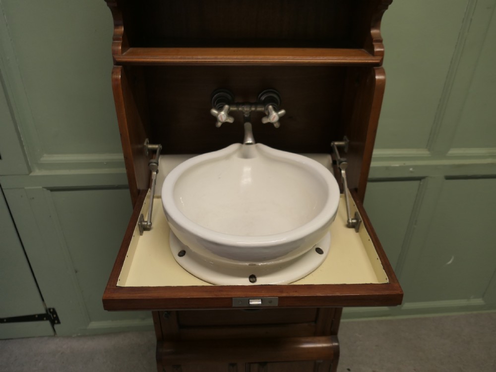 A tall, narrow wooden French marine vanity cabinet featuring a spindled top gallery, a mirrored upper cupboard, small drawers, a drop-front compartment, and lower storage doors. View III