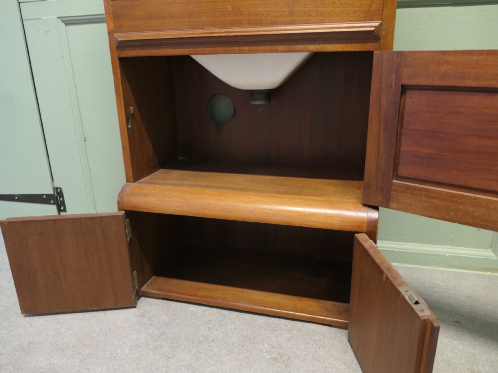 A tall, narrow wooden French marine vanity cabinet featuring a spindled top gallery, a mirrored upper cupboard, small drawers, a drop-front compartment, and lower storage doors. View V