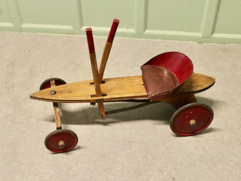 A 1930s hand-operated wooden toy vehicle with a pointed torpedo body, two red-tipped propulsion levers, a curved red seat, and four red wheels.