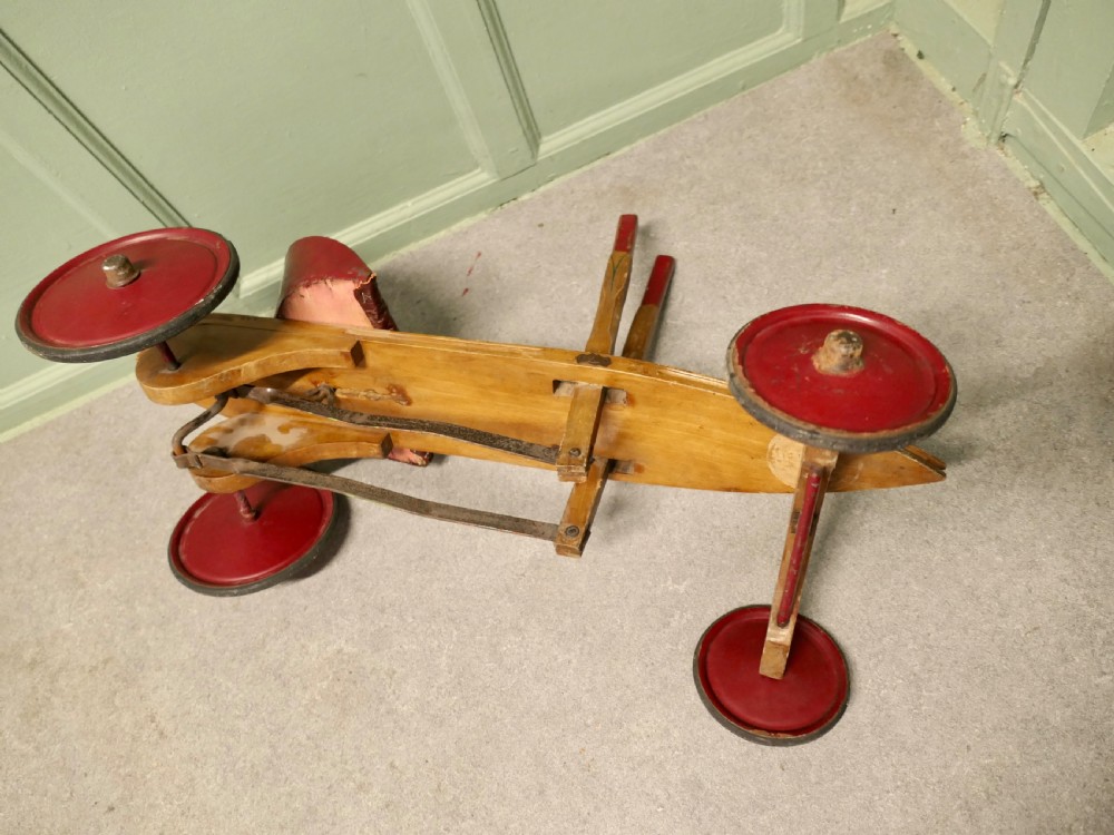 A 1930s hand-operated wooden toy vehicle with a pointed torpedo body, two red-tipped propulsion levers, a curved red seat, and four red wheels. View V
