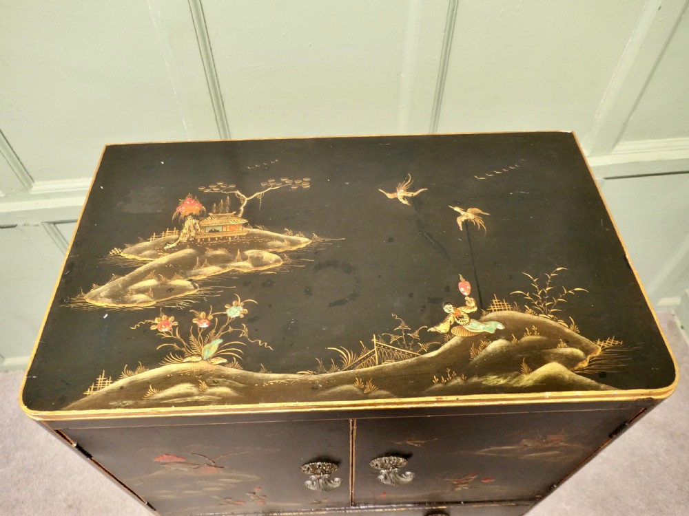 A black lacquered cupboard featuring hand-painted Chinoiserie landscape scenes, two upper doors, two lower drawers, and metal handles. View V