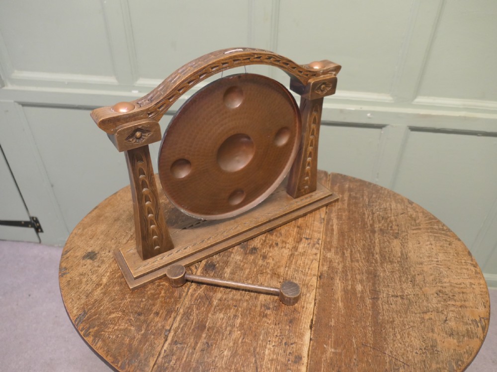 A circular hammered copper gong with raised bosses supported by an arched wooden frame and base with a small striker. View IV