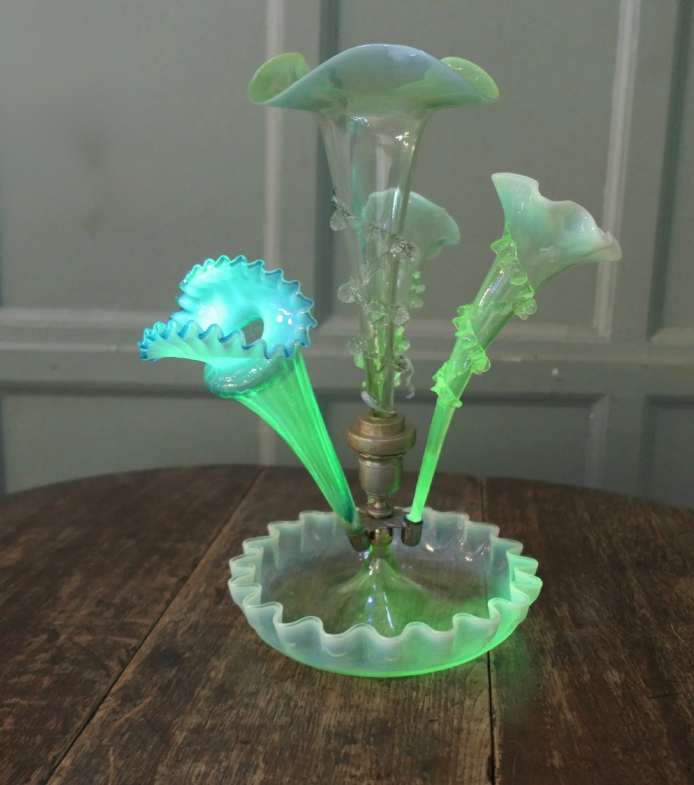 A light green uranium and opalescent glass epergne featuring three trumpet-shaped flower holders with crimped rims set above a ruffled glass dish base.