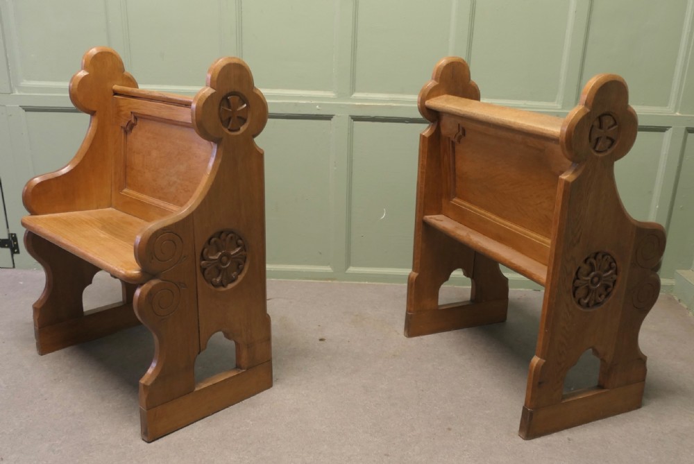 A pair of solid oak Arts and Crafts style hall chairs featuring shaped bench ends, fielded back panels, and gothic cut-outs. View IV