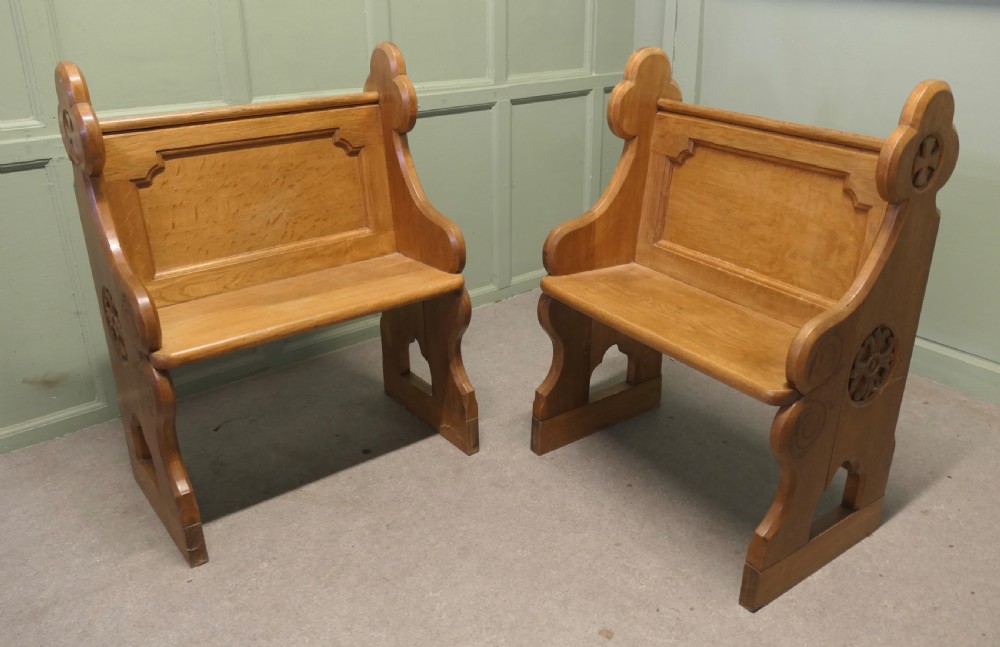 A pair of solid oak Arts and Crafts style hall chairs featuring shaped bench ends, fielded back panels, and gothic cut-outs. View V